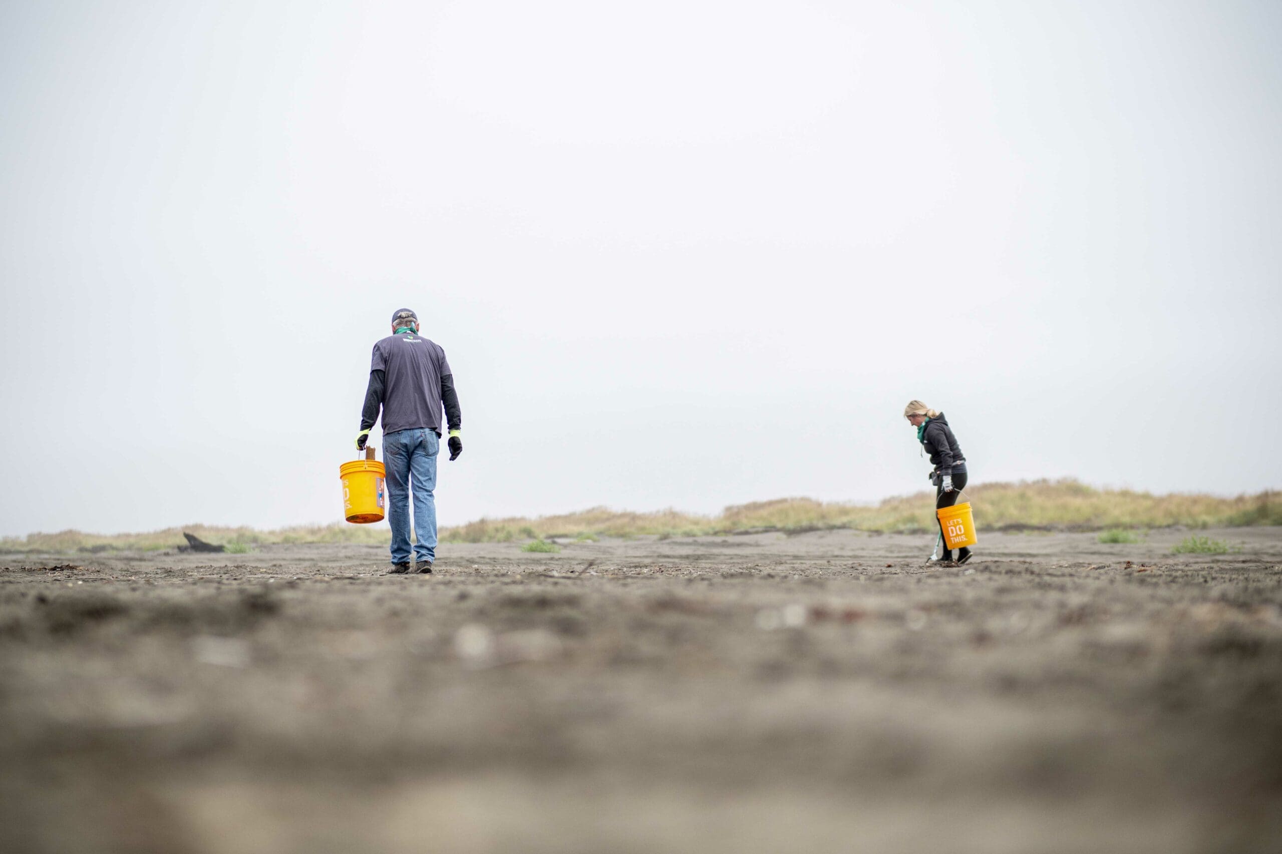 Two people cleaning up trash on coast