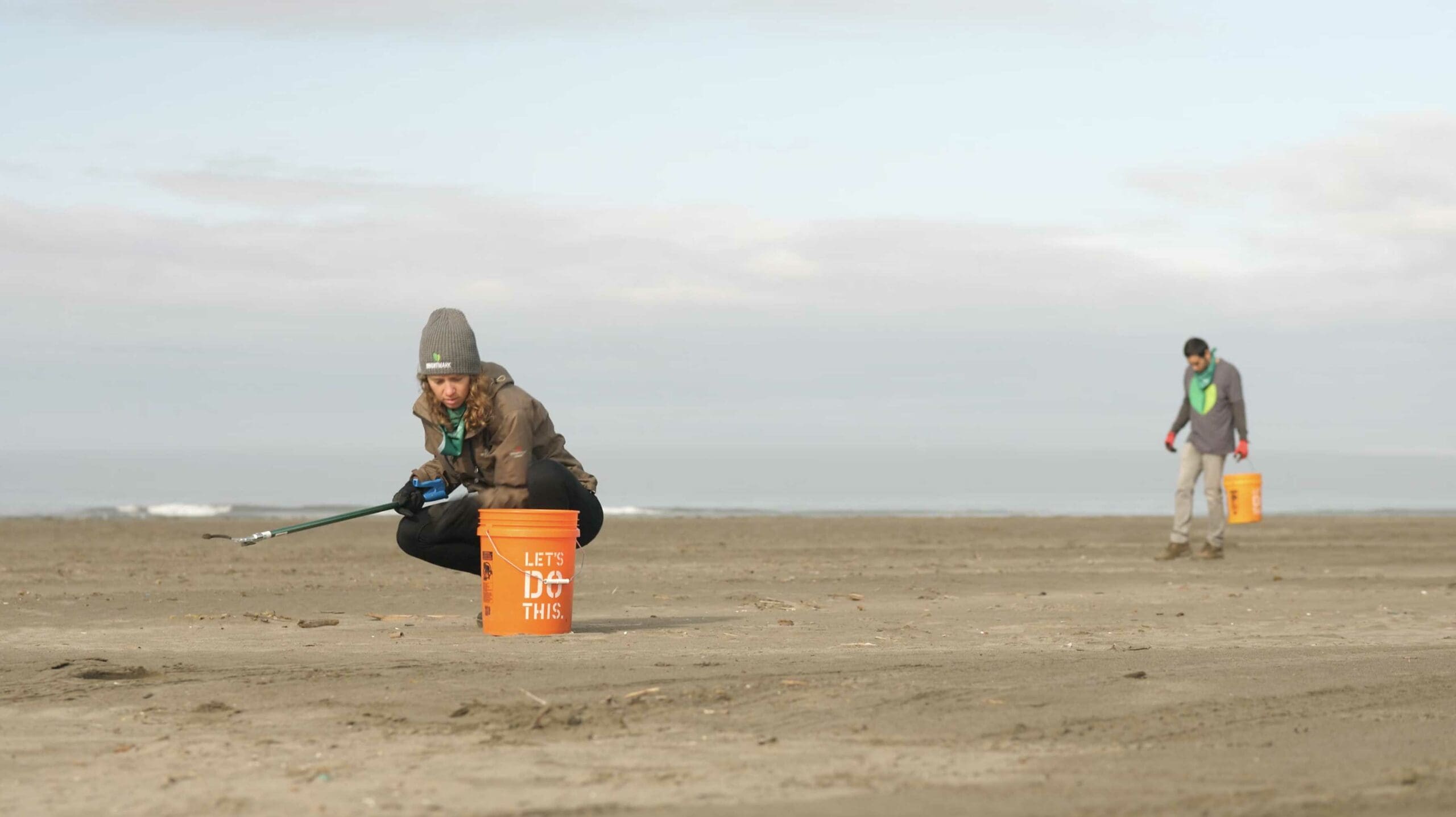 Two people picking up trash on beach