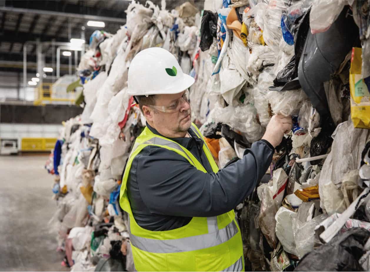 Brightmark worker wearing safety vest and hard hat handling plastic waste.