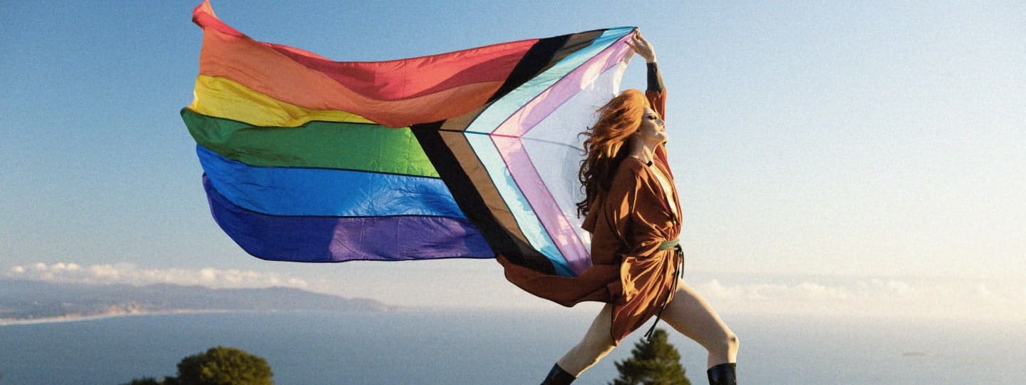 Drag queen holding a Pride flag in the mountains