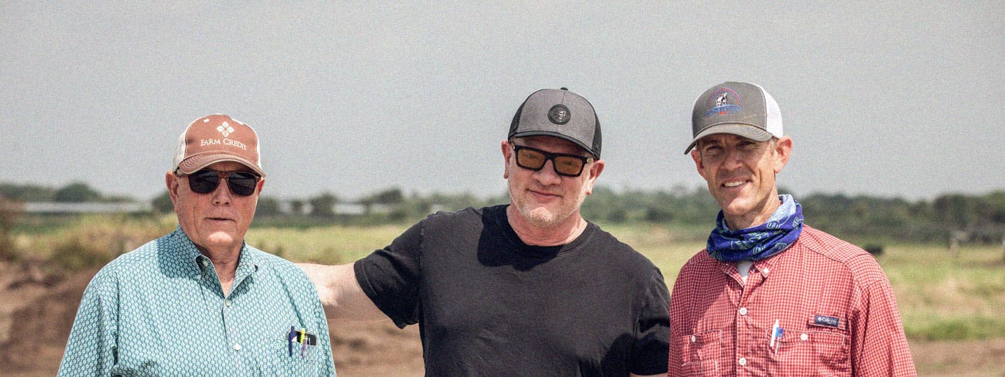 Three men on a farm smiling and posing together for a group shot